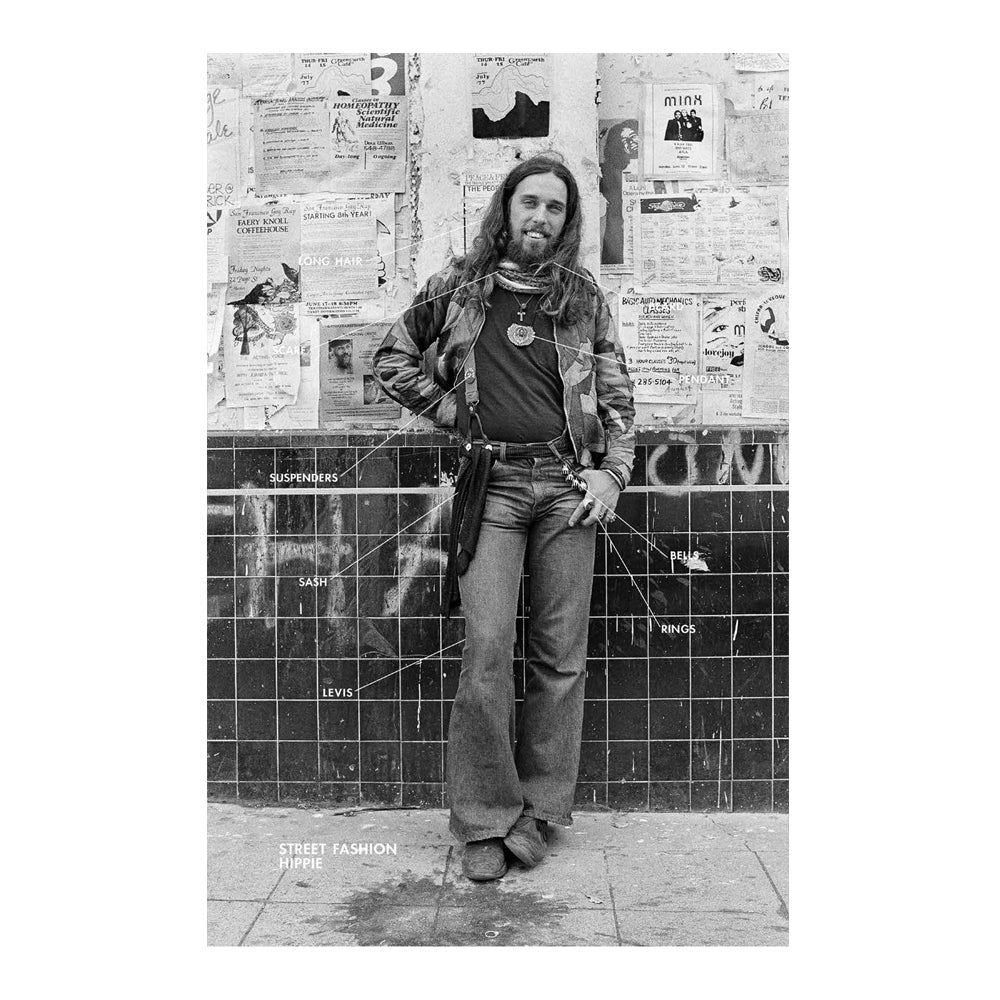 Person wearing a patterned jacket and jeans standing in front of a tiled wall with posters.
