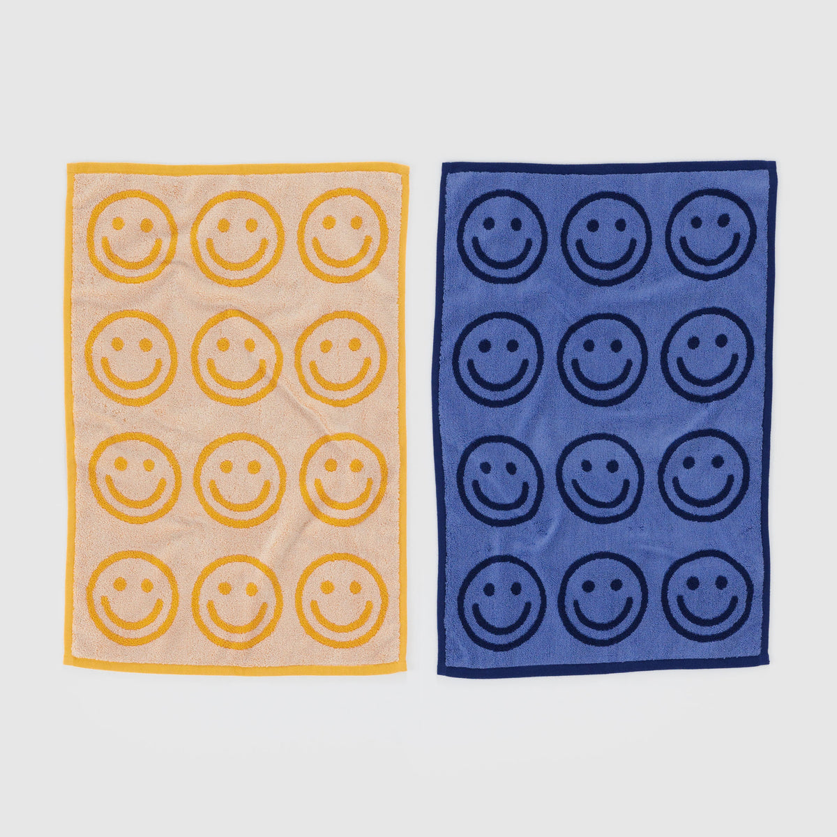 Two towels, one beige with yellow smiley faces and one blue with navy smiley faces, on a light gray background.
