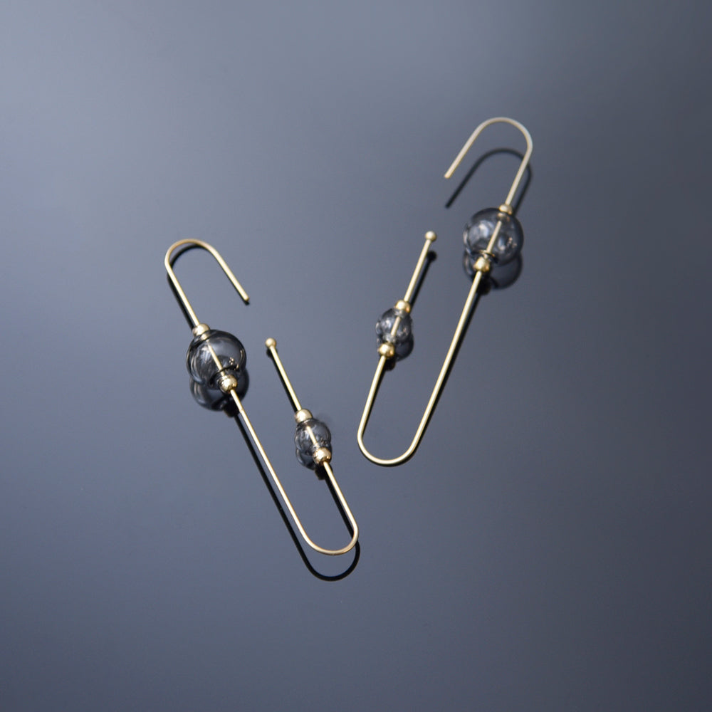 Pair of gold earrings with dark beads on a gradient blue background