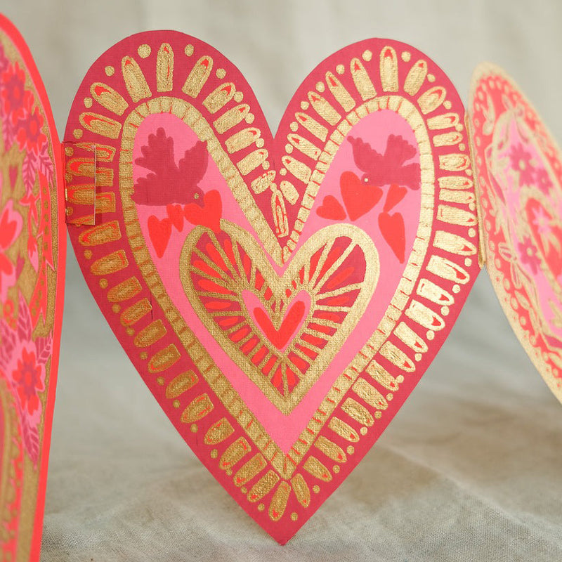 Decorative heart-shaped card with pink and gold design on a textured surface