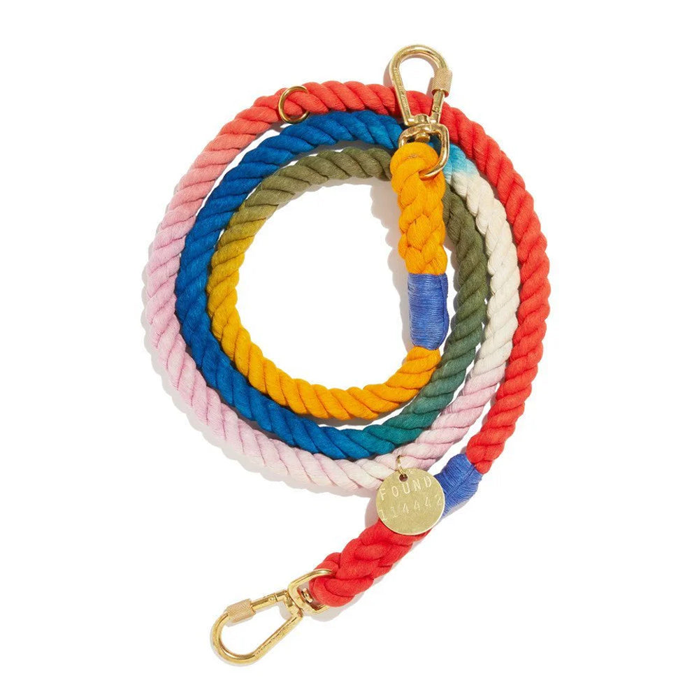 A coiled multicolor braided rope leash with gold-tone metal hardware, including a lobster clasp and a round branded tag. The rope shows multiple color bands: red, pink, light blue, olive green, mustard yellow, and white, with blue wrap accents.