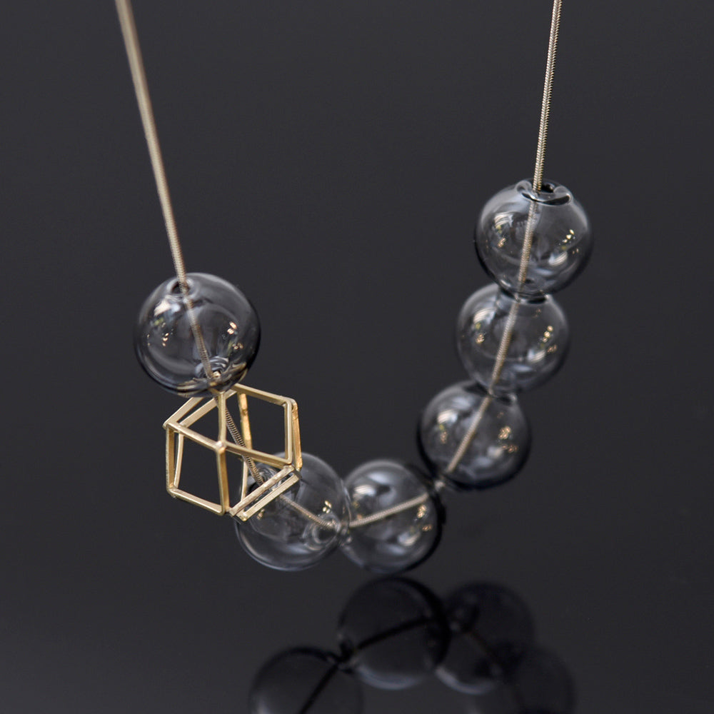 Necklace with grey clear beads and a gold hexagon pendant on a dark background