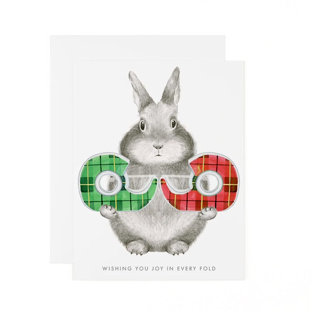Holiday Joy in Every Fold Holiday Card featuring bunny holding two gift wrapping tapes, with white envelope.