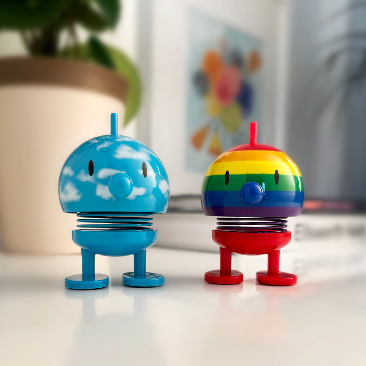 Two colorful Hoptimists, one cloud and one rainbow, on a light surface with a blurred background.