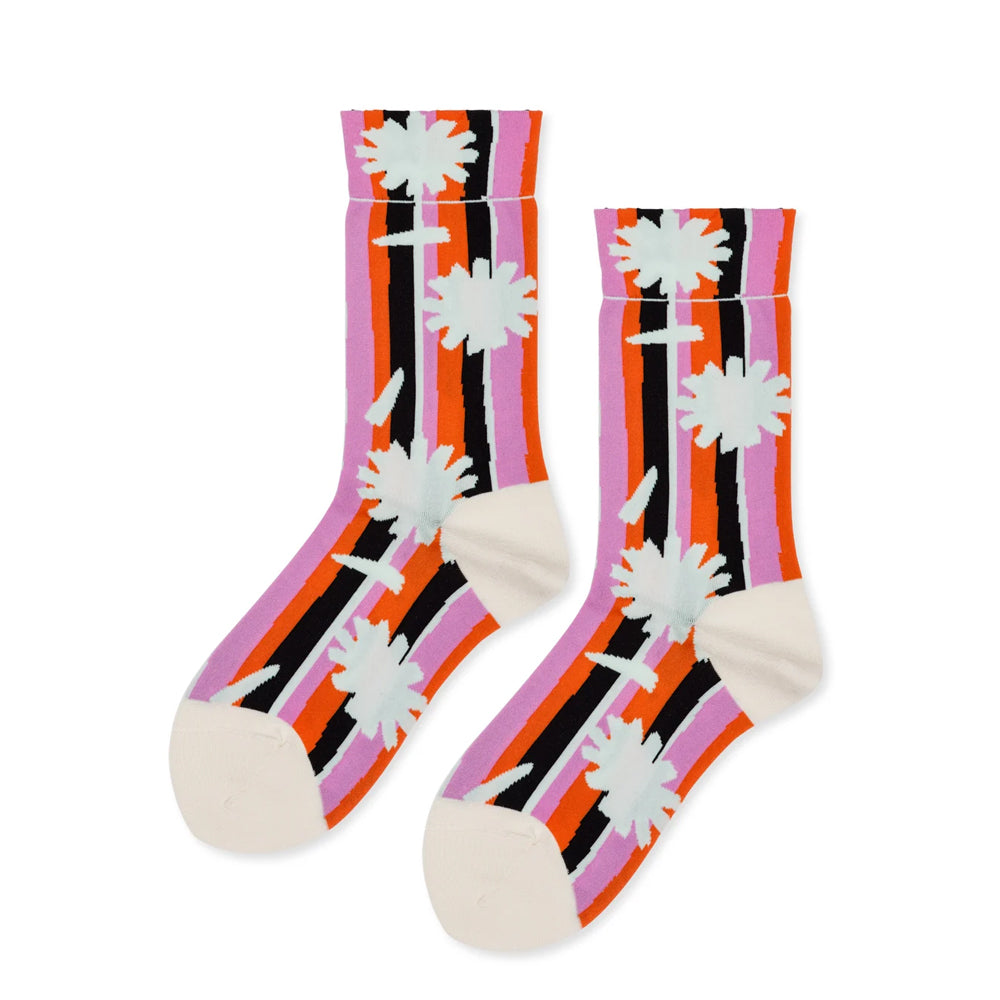 A pair of crew socks with a retro striped pattern in orange, pink, black, and white, featuring stylized daisy flower motifs and cream-colored heels and toes, shown on a plain white background.