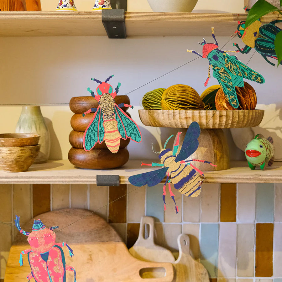 Colorful insect-shaped decorations on a kitchen shelf with tiled wall in the background.