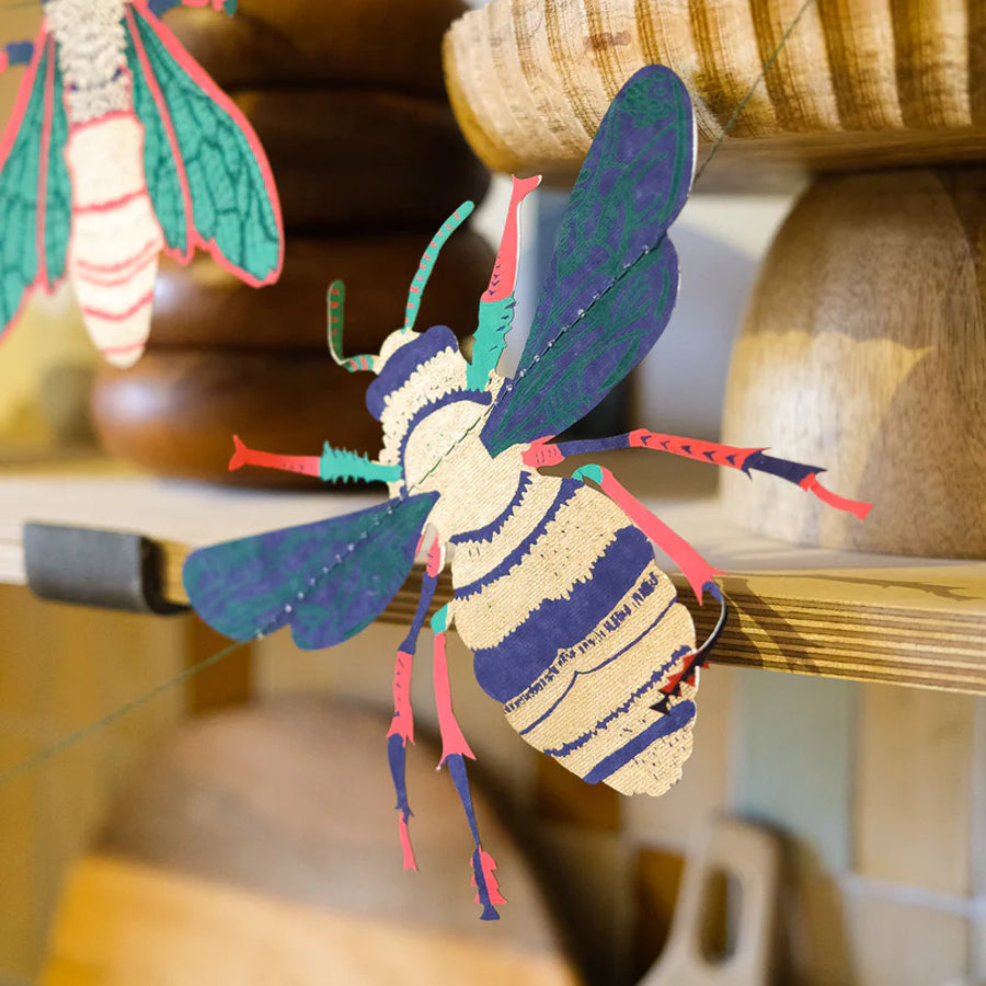 Colorful bee-shaped object on a wooden shelf with blurred background