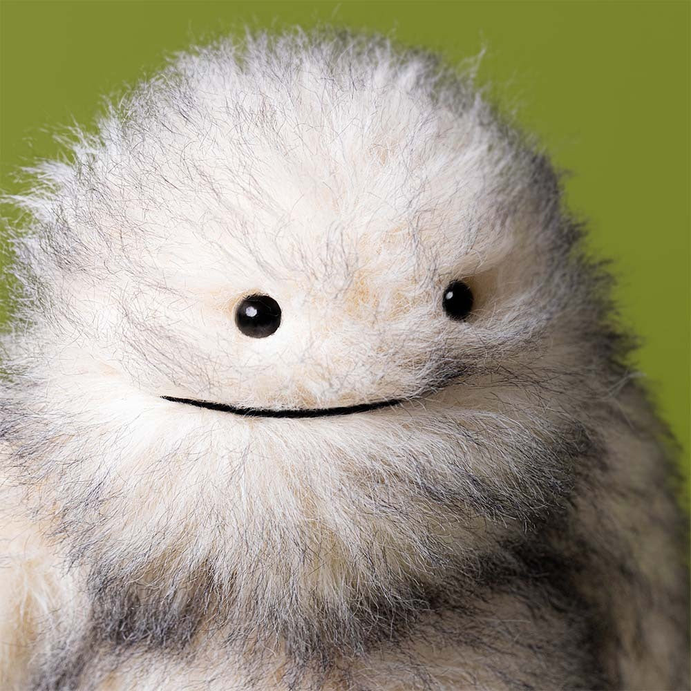 Close-up of a fluffy white creature with black eyes against a green background