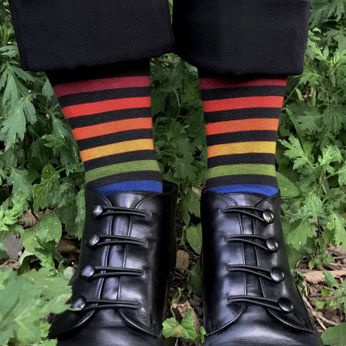 A single crew sock with horizontal rainbow stripes on a black base, shown against a plain white background.