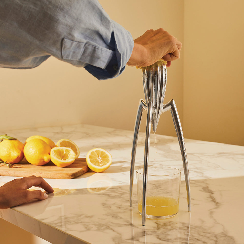 Person using a manual juicer to extract juice from lemons on a marble countertop.