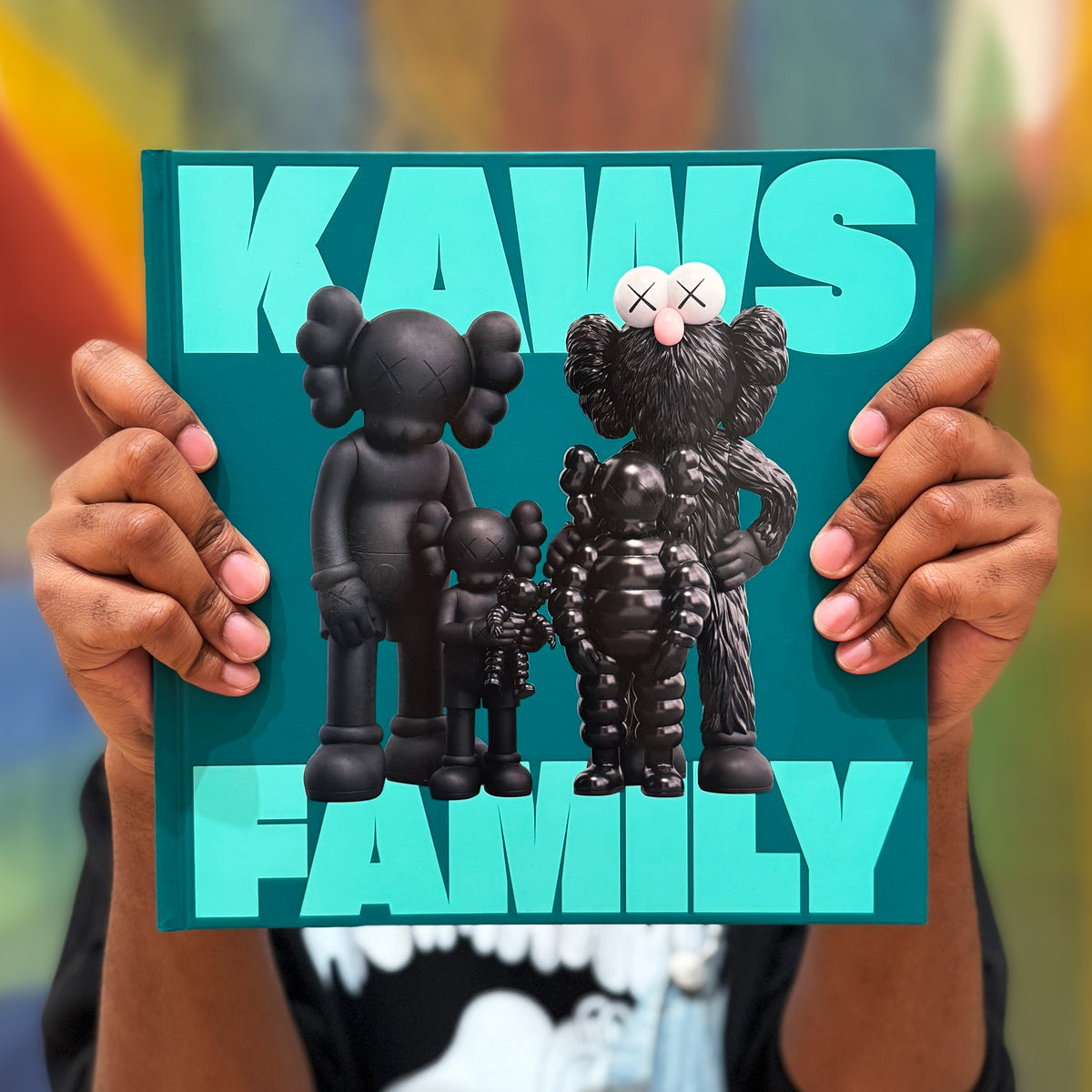 Person holding a KAWS Family book with colorful background