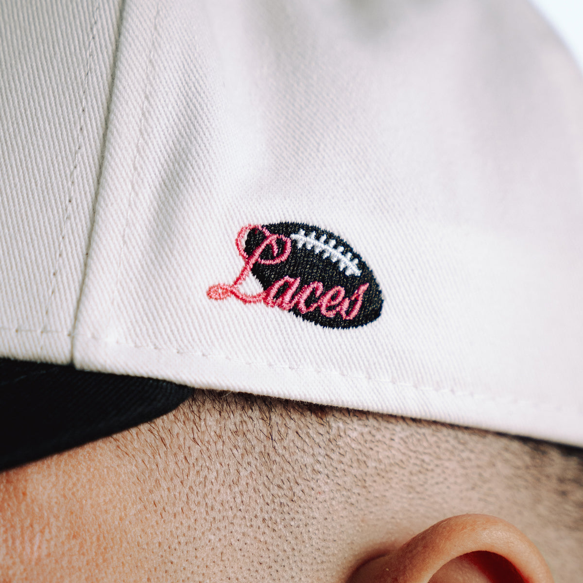 Close-up of a white cap with 'Laces' embroidered on it, worn by a person.