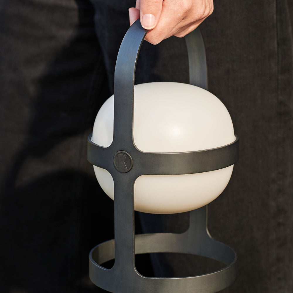 Hand holding a spherical white light fixture with a black metal handle against a dark background