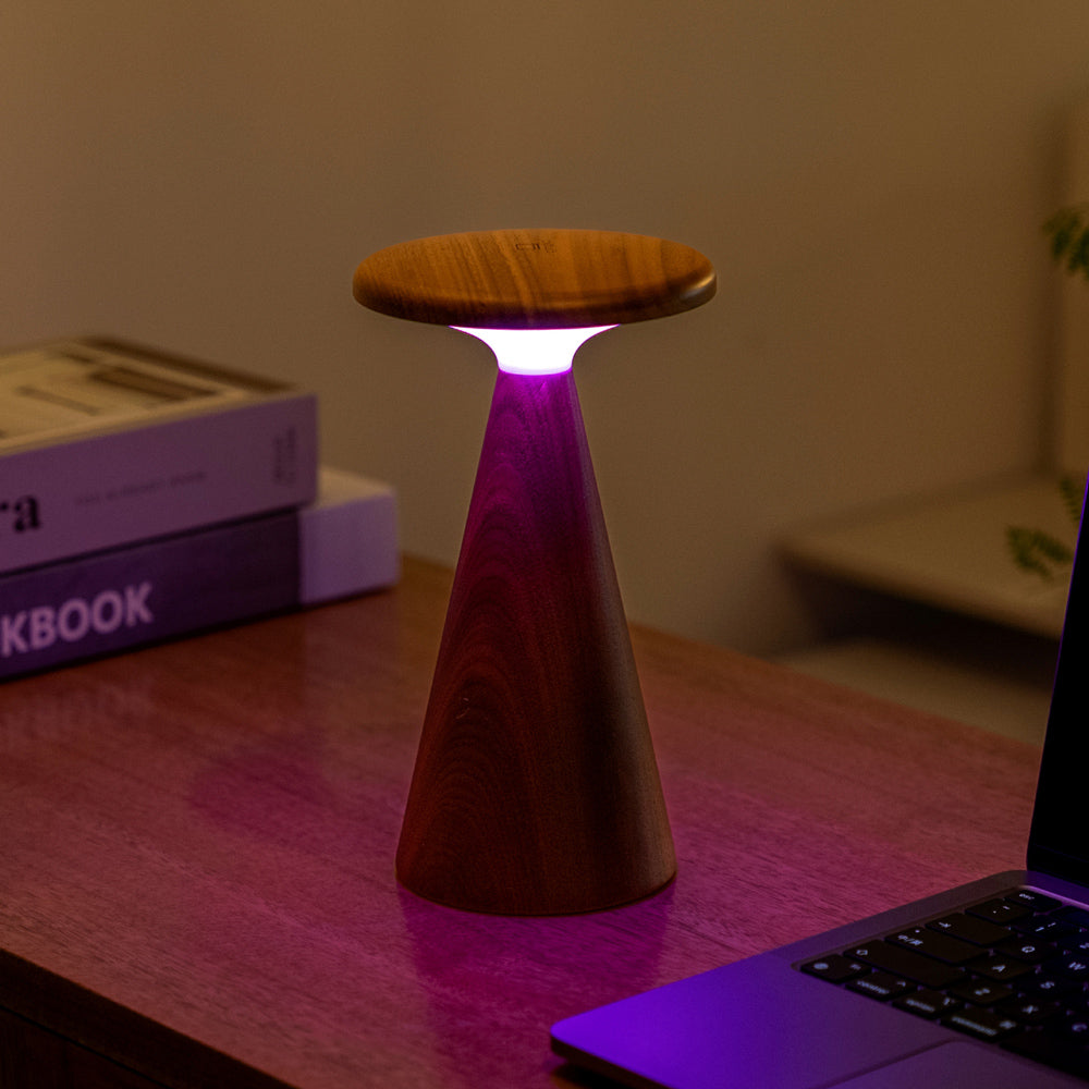 Wooden lamp with purple base on a desk next to a laptop and books