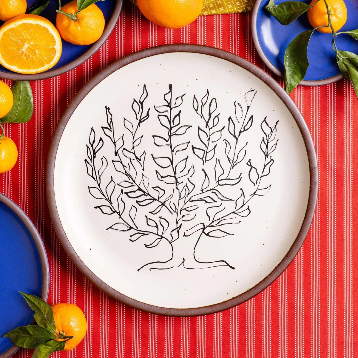 A round ceramic plate with a hand-painted black botanical line drawing of a leafy tree on an off-white background, featuring a contrasting brown rim.