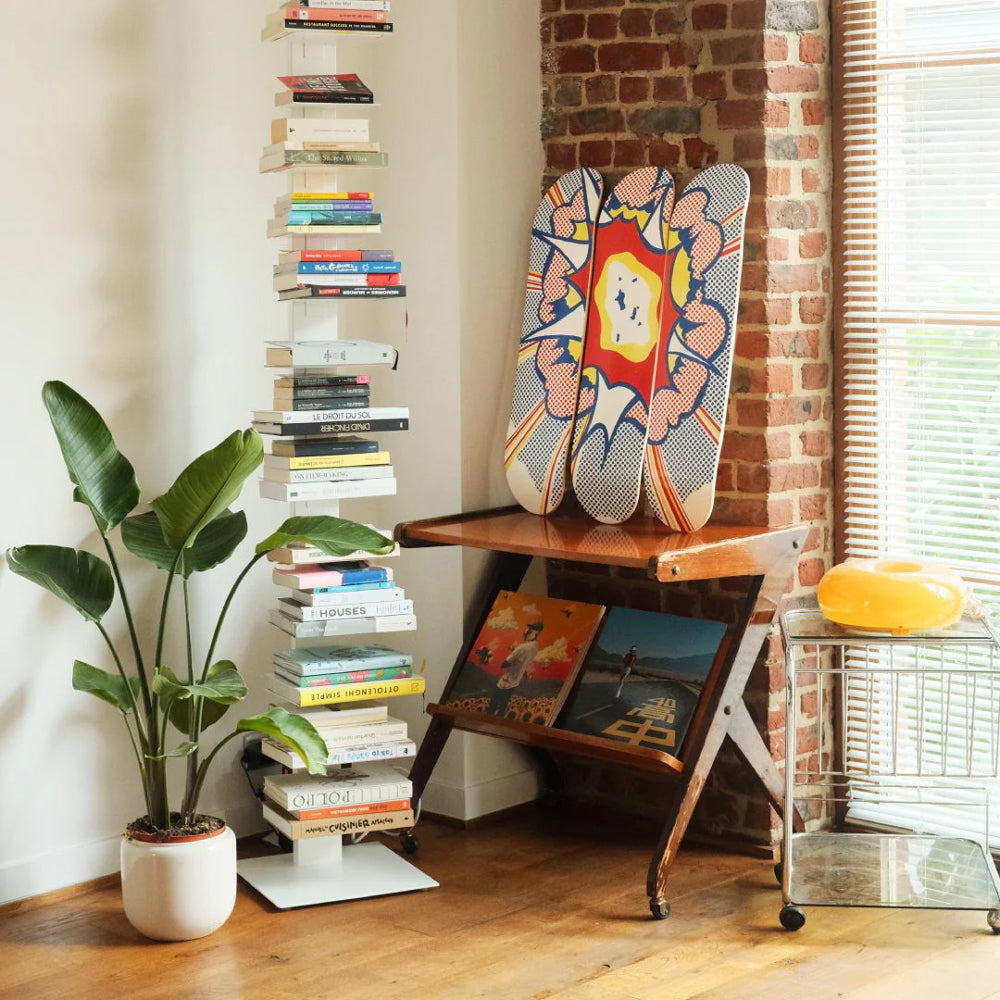 Wooden shelf with books and triptych skateboards against a brick wall.