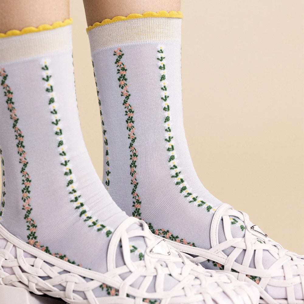 White socks with floral pattern worn with a white sneaker on a beige background