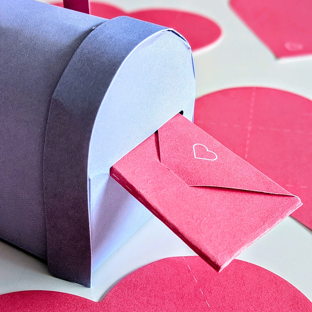 Red envelope with a heart being placed into a purple mailbox on a heart-patterned background.