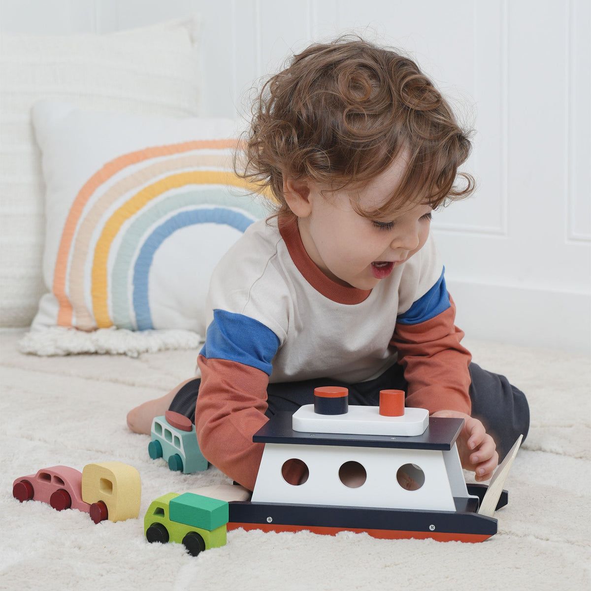 Child playing with a toy boat and cars on a white blanket