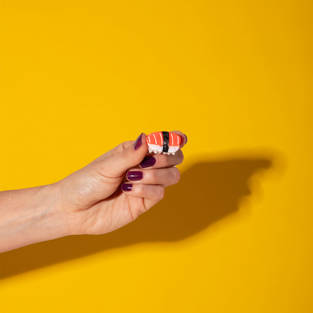 Hand holding a small sushi hair claw against a yellow background