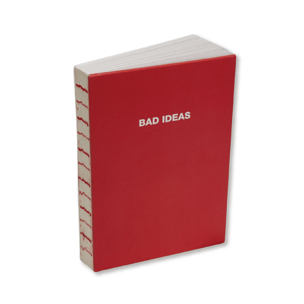 A hardcover notebook with a red cover and white pages, standing upright at a slight angle. The front cover features the text 'BAD IDEAS' in white, and the spine shows red stitching along the edges.