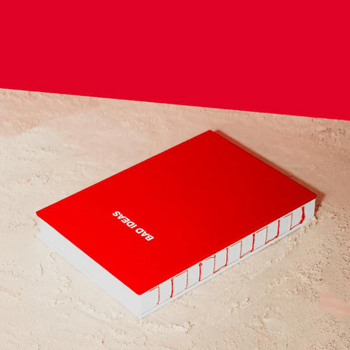 A hardcover notebook with a vibrant red cover and white pages, lying on a textured beige surface with a solid red background.