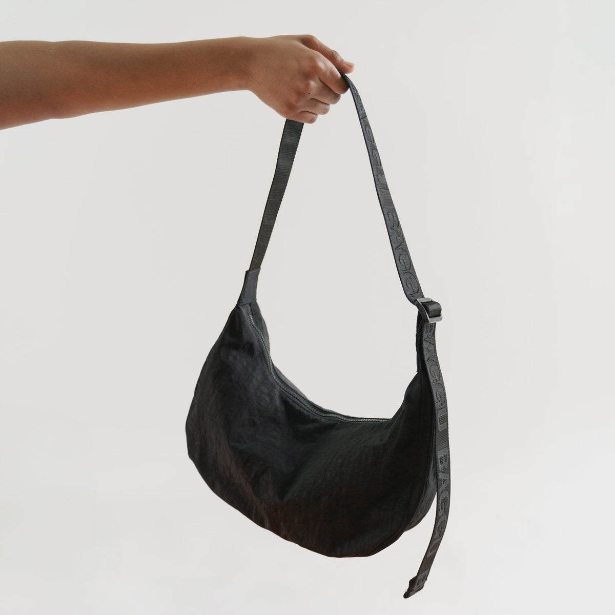 Black shoulder bag held by a hand against a light gray background