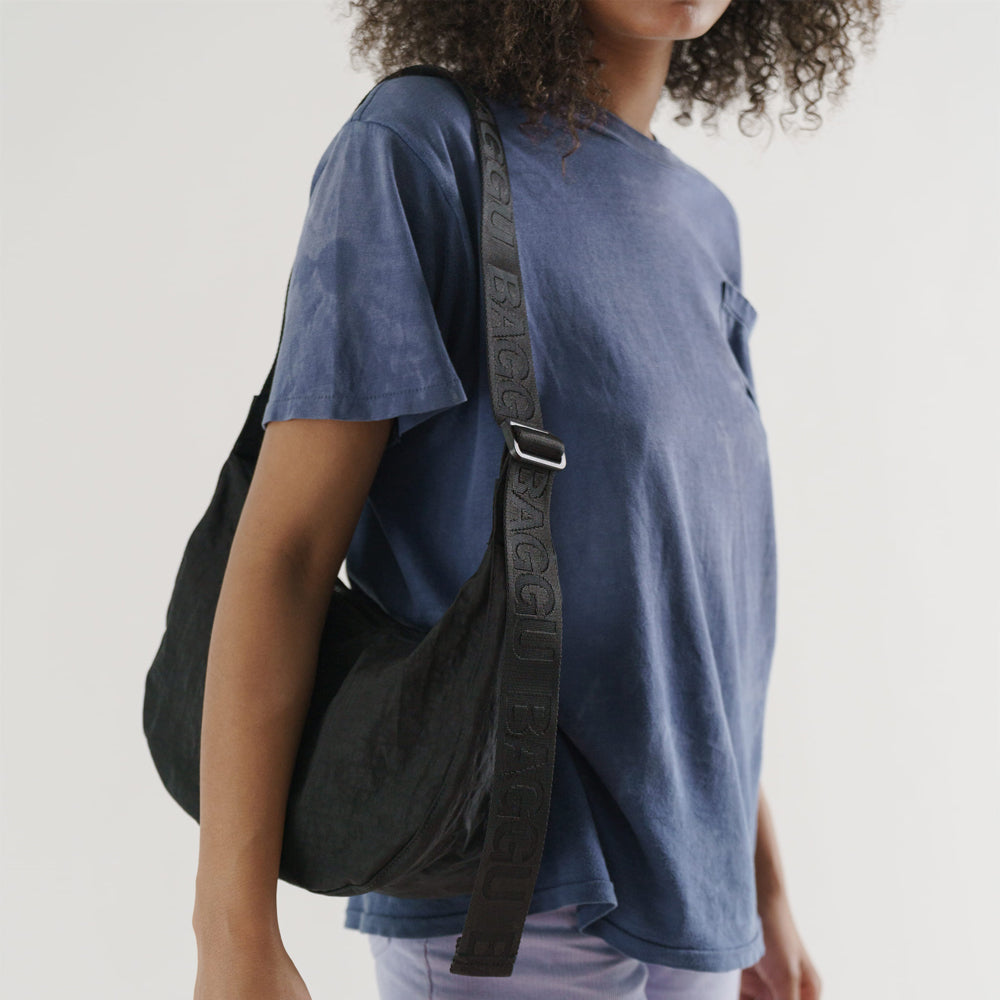 Person wearing a blue shirt with a black bag over one shoulder on a plain background