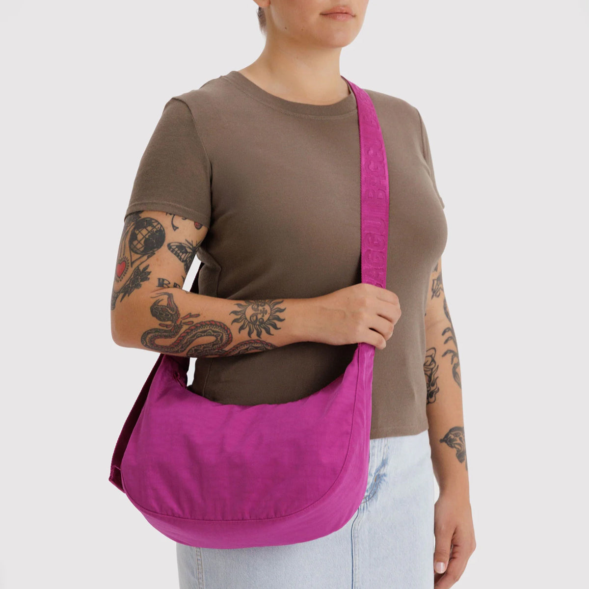 Person wearing a brown shirt and light blue jeans with a pink shoulder bag on a white background
