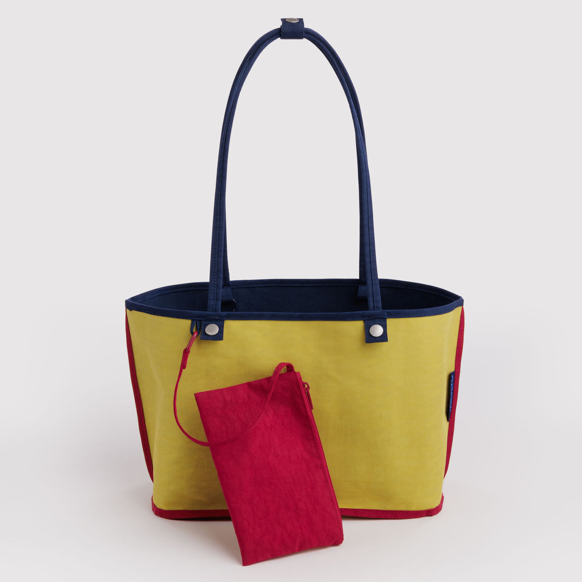 A yellow tote bag with navy blue handles and trim, shown with a small red zippered pouch in front, on a light gray background.