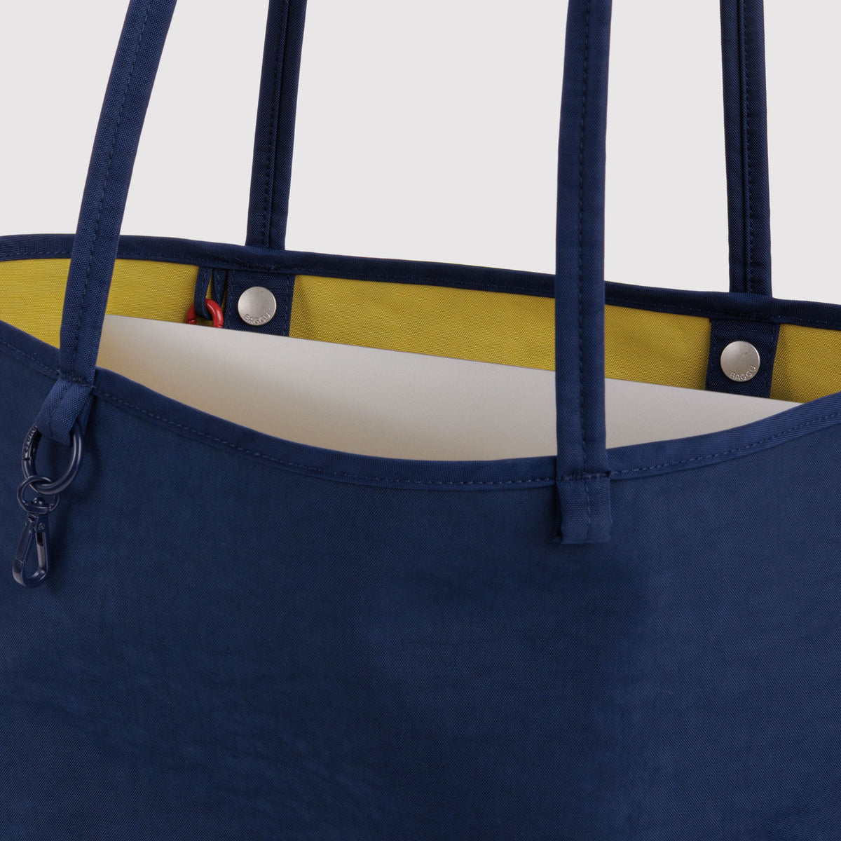Close-up of a navy blue tote bag with a yellow interior lining and silver-tone hardware, including a zipper pull and metal rivets.