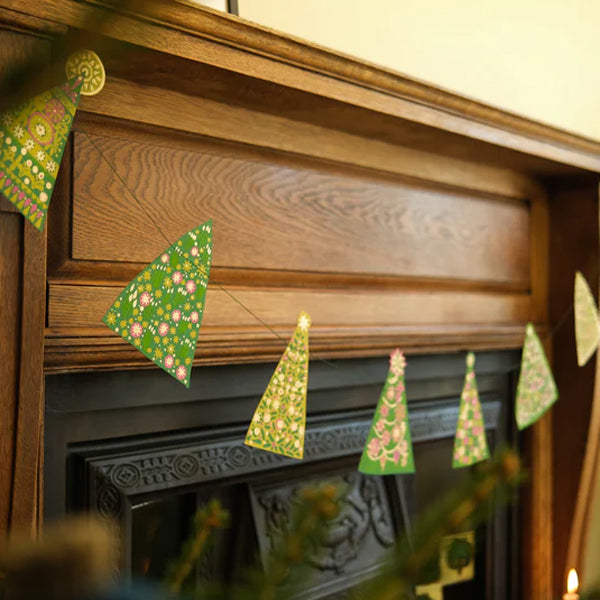 Decorative paper Christmas trees hanging on a wooden mantelpiece.
