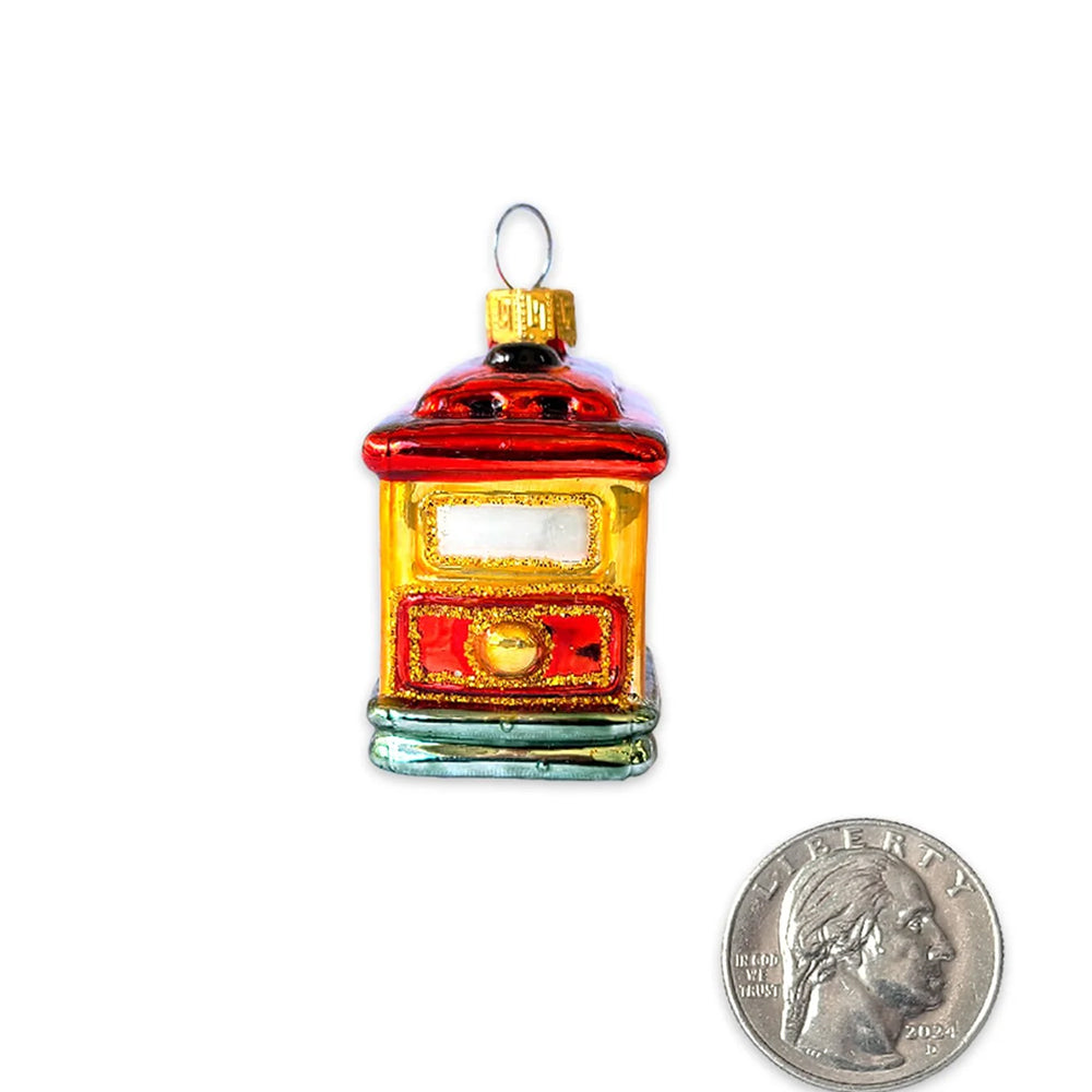 A small glass trolley ornament with a red roof, gold body, and green base, shown next to a U.S. quarter.