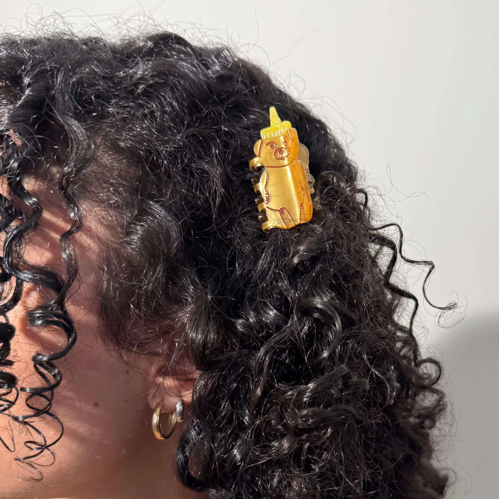 Close-up of a person's hair with a gold hair clip featuring a honey bear design.