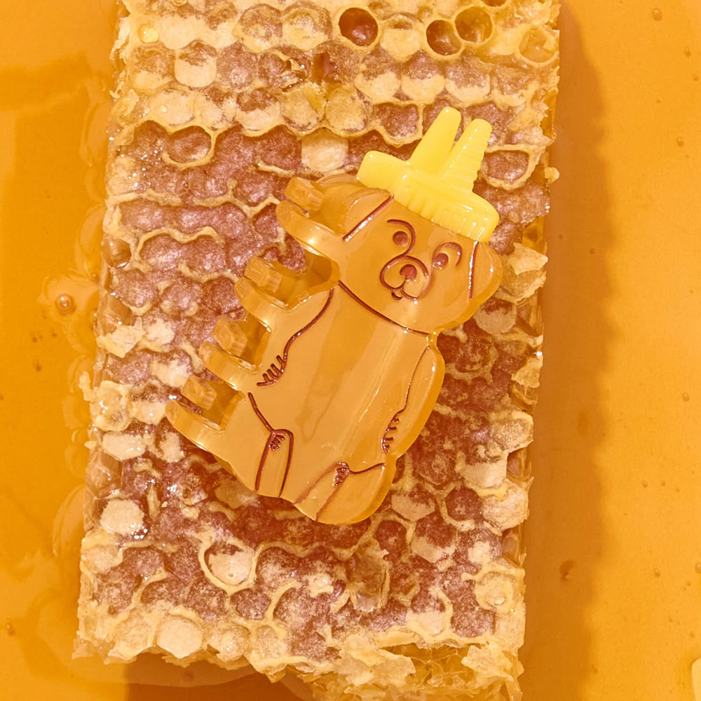Yellow bear-shaped honey bottle hair claw on a honeycomb background
