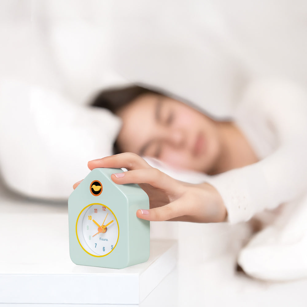 Person in bed with a small house-shaped alarm clock