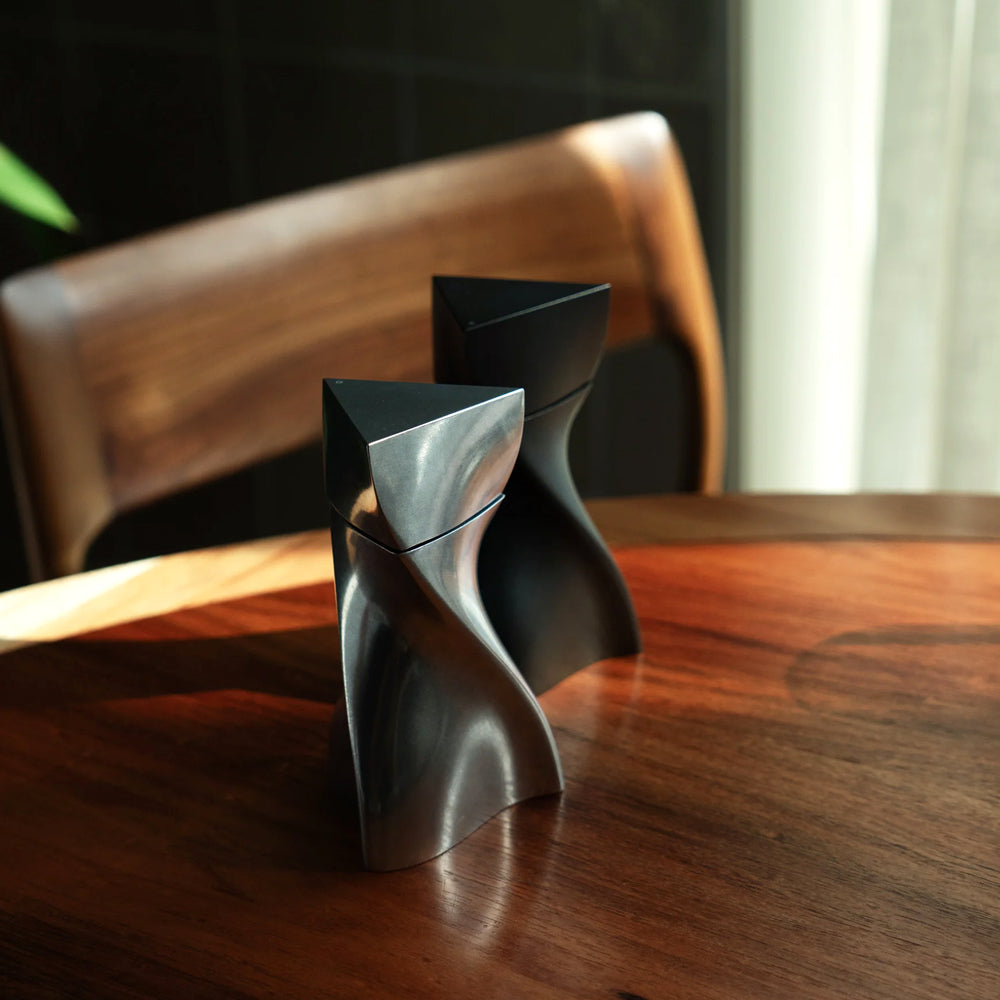 Black geometric salt and pepper grinders on a wooden table with a blurred background