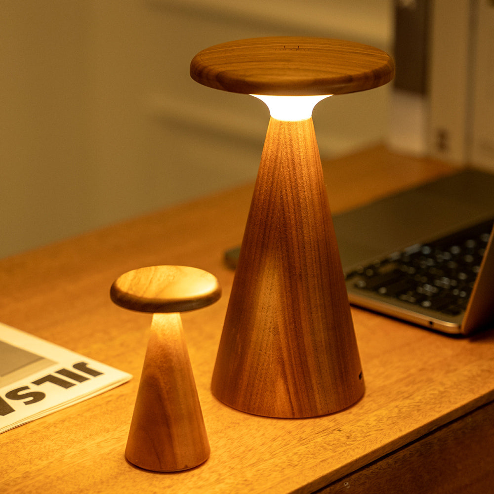 Wooden lamp with a warm glow on a desk next to a keyboard and newspaper.
