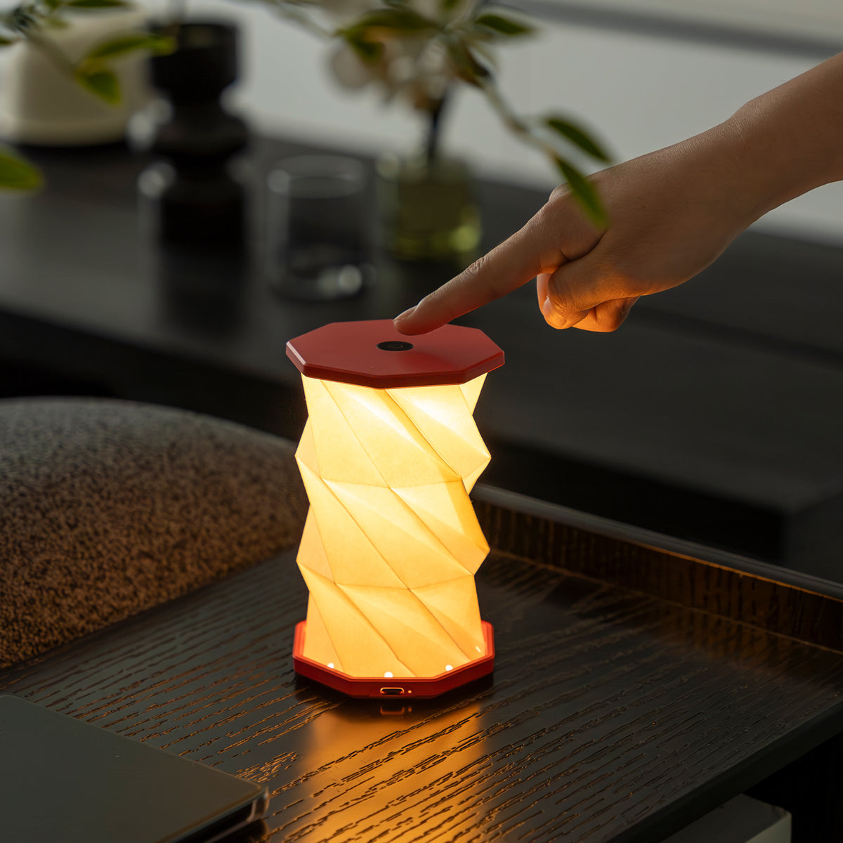 Hand pressing a button on a red and white portable lamp on a dark surface.