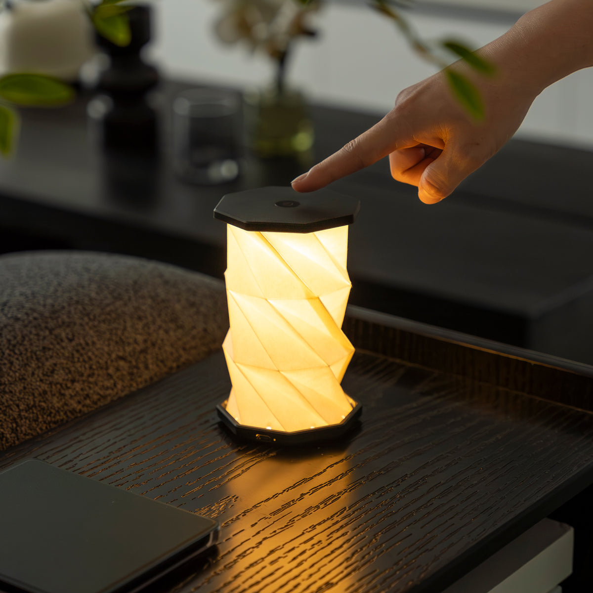 Hand pressing a button on a small, glowing lamp on a dark surface.