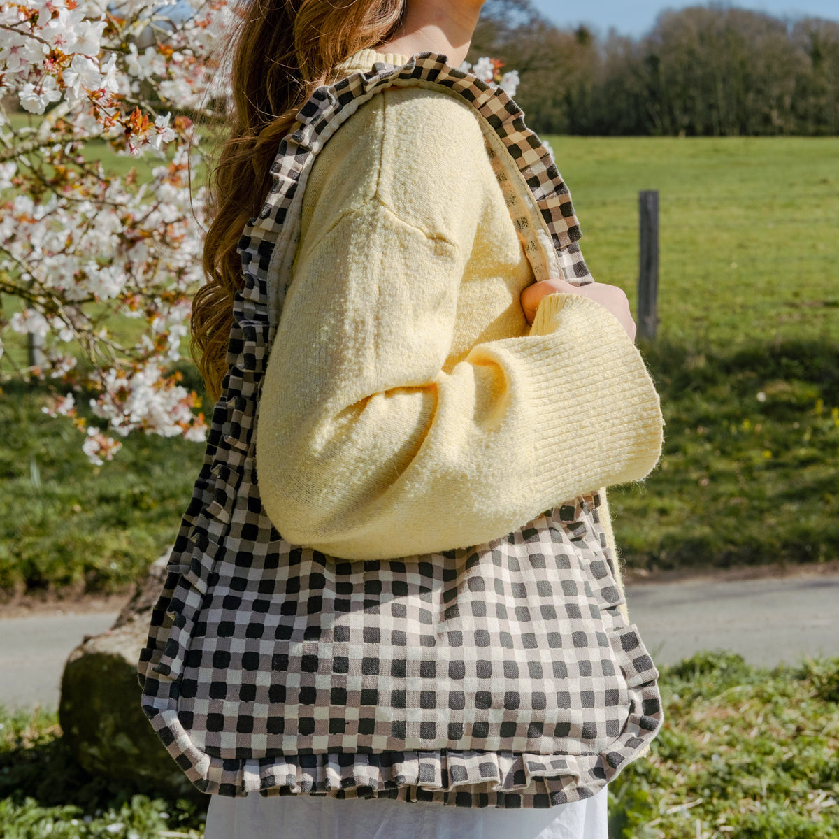 Person holding momo bag, standing outdoors near a flowering tree.