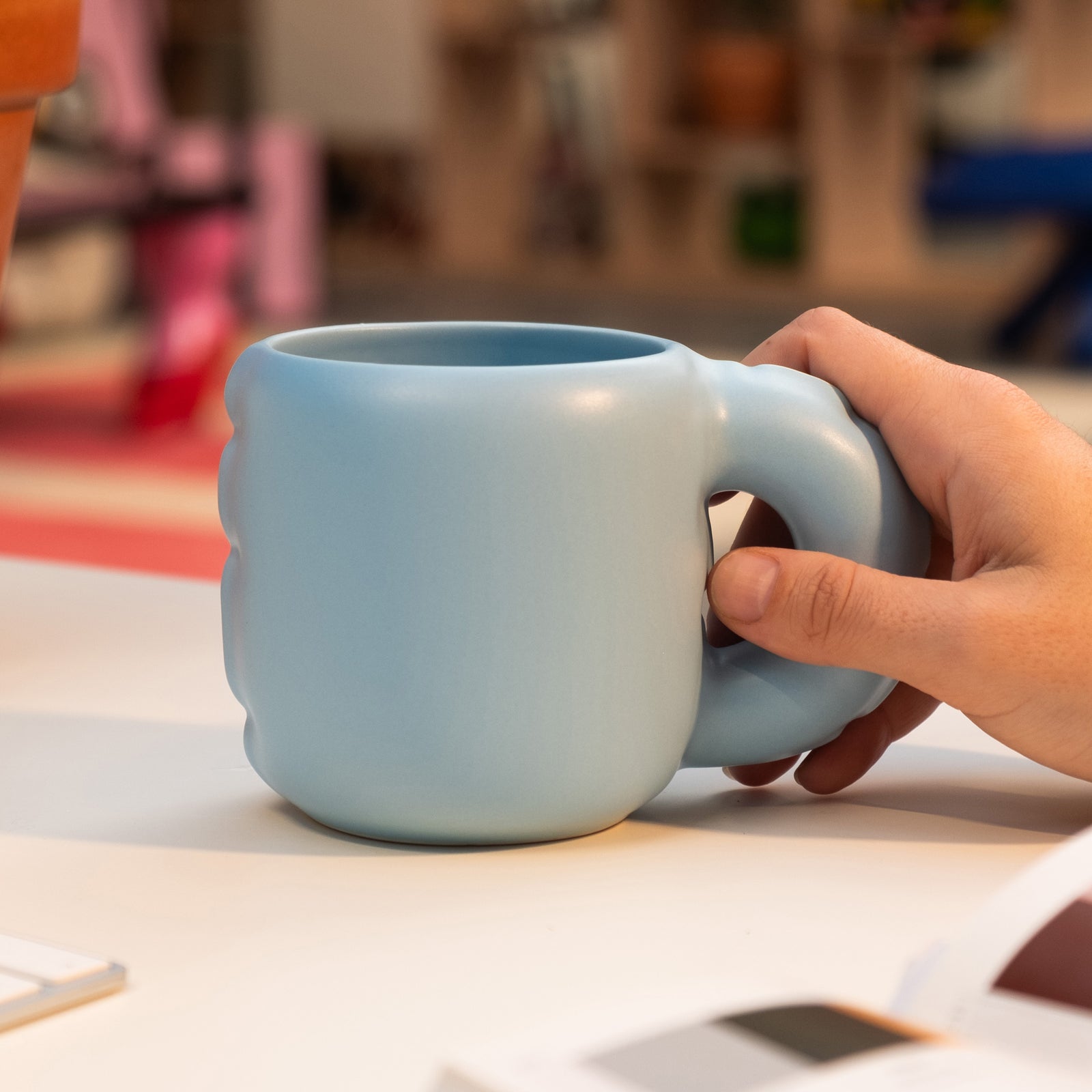 A light blue ceramic mug with a unique, integrated loop handle, shown on a plain white background.