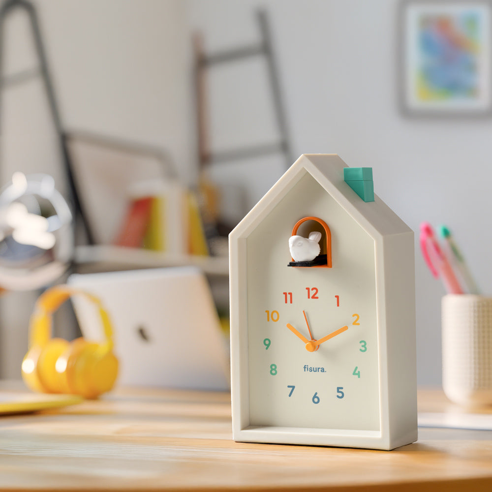 House-shaped clock with a bird figurine on a wooden surface