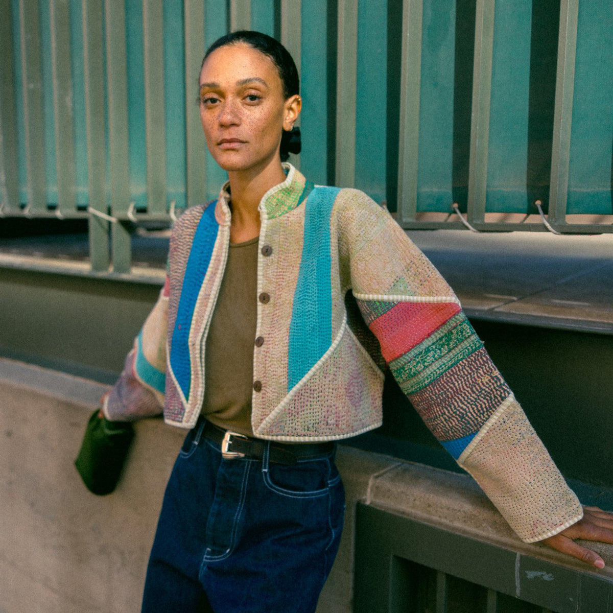 Woman wearing a colorful quilted patch sweater leaning against a wall.