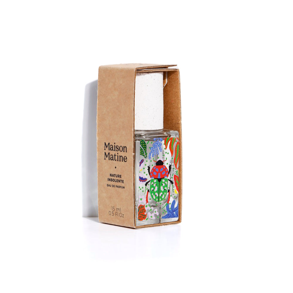 Maison Matine Nature Insolente Eau de Parfum in a clear glass bottle with a colorful illustrated label, standing next to its brown kraft paper packaging box on a white background.