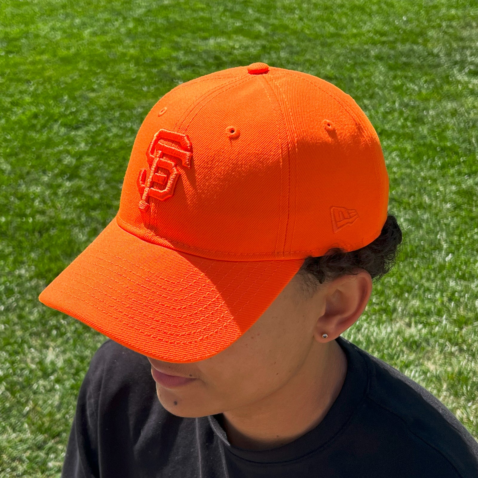Person wearing an orange cap with a logo on a grassy background