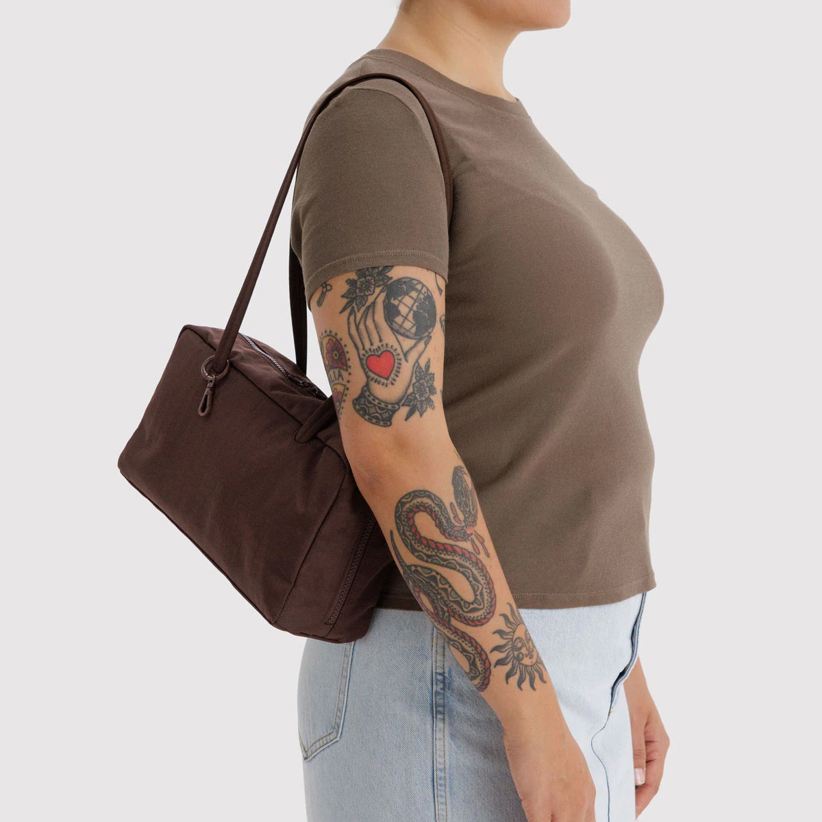Person wearing a brown shirt and light blue jeans, holding a brown bag on a white background