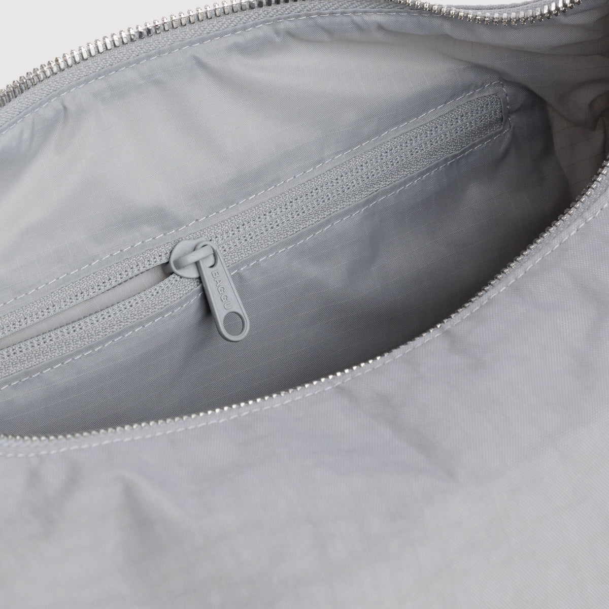 Close-up of the interior of a light gray nylon bag, showing a zippered pocket with a matching gray zipper pull.