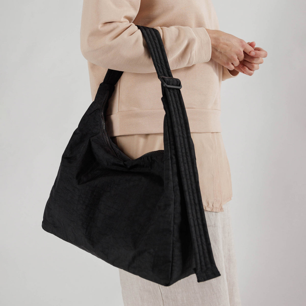Person holding a black shoulder bag against a plain background