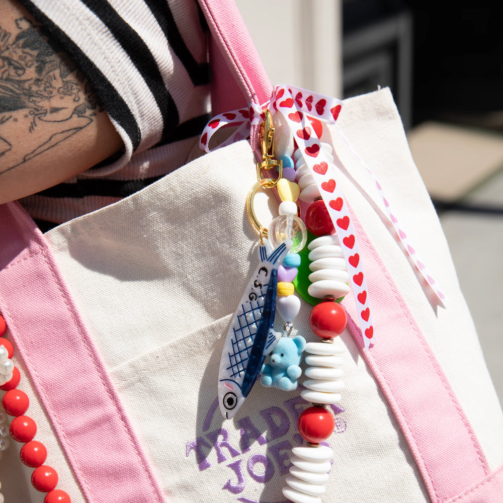 Colorful beaded keychain with charms on a pink and white bag.